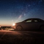 Um carro parado com os farois iluminando um homem sentado.