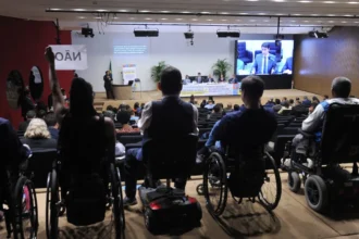 Pessoas com deficiência, muitas em cadeiras de rodas, participam de uma audiência pública em um auditório.