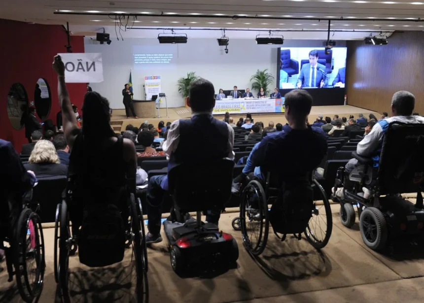 Pessoas com deficiência, muitas em cadeiras de rodas, participam de uma audiência pública em um auditório.