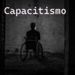 Pessoa em uma cadeira de rodas está de costas, sozinha, em um cômodo escuro e deteriorado. No alto a palavra capacitismo em letras brancas.