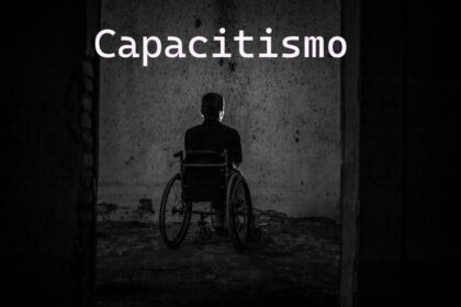 Pessoa em uma cadeira de rodas está de costas, sozinha, em um cômodo escuro e deteriorado. No alto a palavra capacitismo em letras brancas.