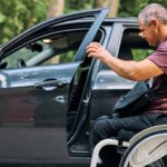 Homem cadeirante ao lado de um carro, abrindo a porta do veículo.