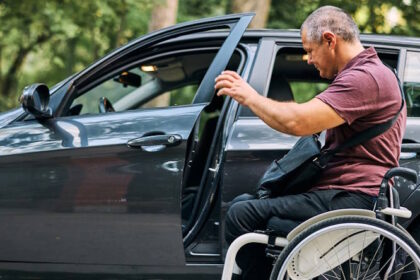 Homem cadeirante ao lado de um carro, abrindo a porta do veículo.