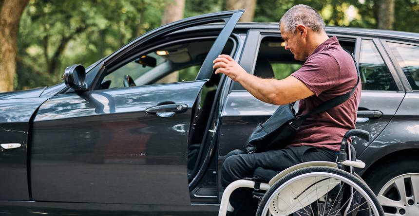 Homem cadeirante ao lado de um carro, abrindo a porta do veículo.