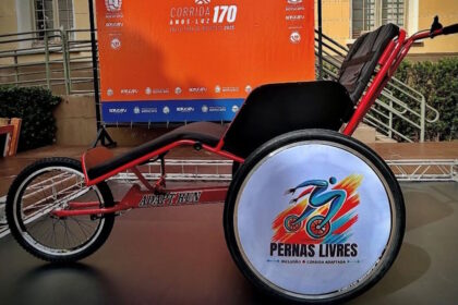 Uma cadeira de rodas adaptada para corridas com a logo do projeto Pernas Livres no centro da roda traseira.
