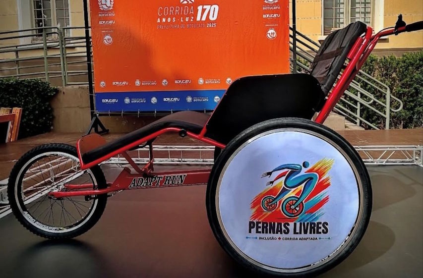 Uma cadeira de rodas adaptada para corridas com a logo do projeto Pernas Livres no centro da roda traseira.