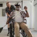 Homem em cadeira de rodas remando usando óculos de realidade virtual, acompanhado por outro homem.