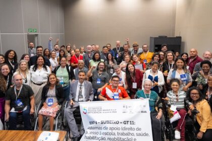 Grupo diverso de pessoas, incluindo pessoas com deficiência e usuários de cadeira de rodas, posa sorridente para a foto durante o 5º Fórum Nacional dos Direitos da Pessoa com Deficiência, realizado em Brasília, de 14 a 17 de julho de 2024. Ao centro, uma faixa destaca o tema do grupo de trabalho: “Sistemas de apoio – direito de acesso à escola, trabalho, saúde, habilitação, reabilitação”.