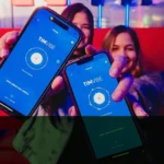 Duas mulheres sorrindo seguram celulares com o aplicativo TIM Vibe aberto, em um ambiente colorido com luzes neon. As telas dos aparelhos exibem a frase “Para vibrar com a música”