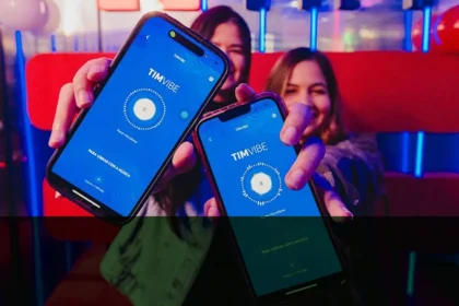 Duas mulheres sorrindo seguram celulares com o aplicativo TIM Vibe aberto, em um ambiente colorido com luzes neon. As telas dos aparelhos exibem a frase “Para vibrar com a música”