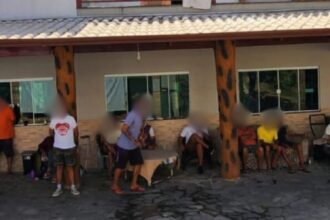 Grupo de pessoas sentadas e em pé em frente a uma construção com varanda e pilares.