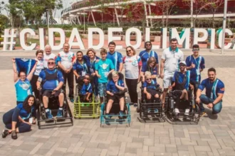 Uma foto de grupo ao ar livre de aproximadamente 20 pessoas, incluindo atletas em cadeiras de rodas motorizadas adaptadas para Power Soccer (Futebol em Cadeira de Rodas) e membros da equipe de apoio ou familiares.