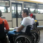 Grupo de homens cadeirantes aguardando em frente a um ônibus de transporte público.