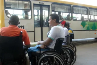 Grupo de homens cadeirantes aguardando em frente a um ônibus de transporte público.