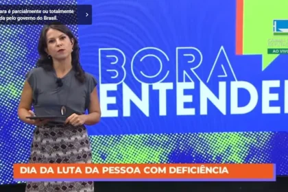 Apresentadora da TV Câmara durante o programa ‘Bora Entender’. No rodapé da tela, uma faixa laranja traz a mensagem: ‘Dia da Luta da Pessoa com Deficiência’. Ao fundo, o painel colorido do programa com o título em destaque.