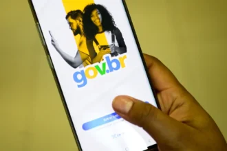 Pessoa segurando um celular que exibe a tela inicial do aplicativo Gov.br, com o logotipo colorido e a opção de login