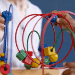 Um plano fechado mostra as m&atilde;os de duas pessoas interagindo com um labirinto de arame colorido, um brinquedo terap&ecirc;utico ou educativo frequentemente usado no desenvolvimento infantil.