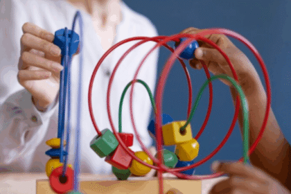 Um plano fechado mostra as mãos de duas pessoas interagindo com um labirinto de arame colorido, um brinquedo terapêutico ou educativo frequentemente usado no desenvolvimento infantil.