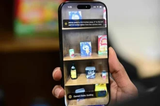 Pessoa segura um smartphone que identifica produtos em uma prateleira usando tecnologia de acessibilidade por IA.