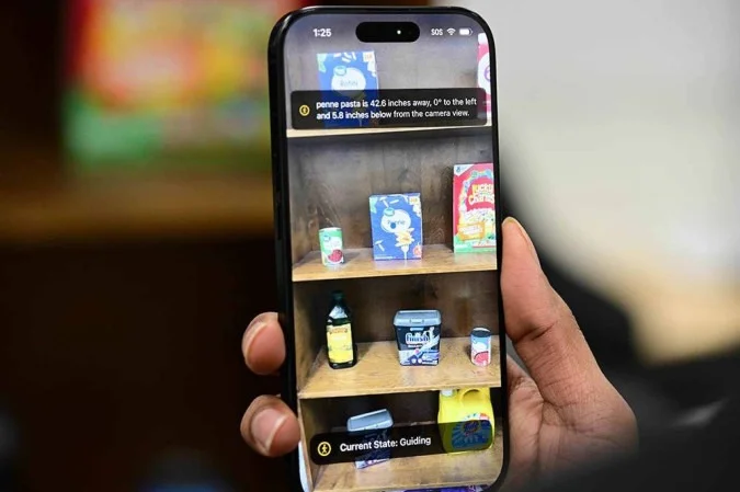 Pessoa segura um smartphone que identifica produtos em uma prateleira usando tecnologia de acessibilidade por IA.