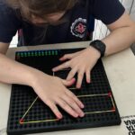 Estudante utiliza material tátil com pinos e elásticos para formar figuras geométricas em atividade educativa.