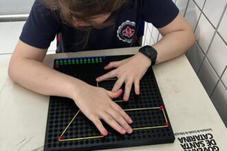 Estudante utiliza material tátil com pinos e elásticos para formar figuras geométricas em atividade educativa.