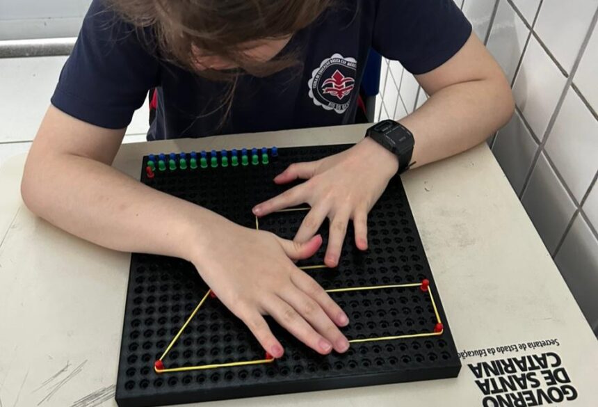 Estudante utiliza material tátil com pinos e elásticos para formar figuras geométricas em atividade educativa.