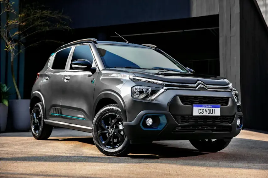 Carro Citroën C3 cinza estacionado em frente a prédio moderno, visto em ângulo frontal.