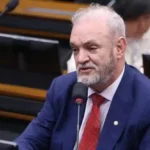 Homem de terno falando ao microfone durante audiência em comissão parlamentar.