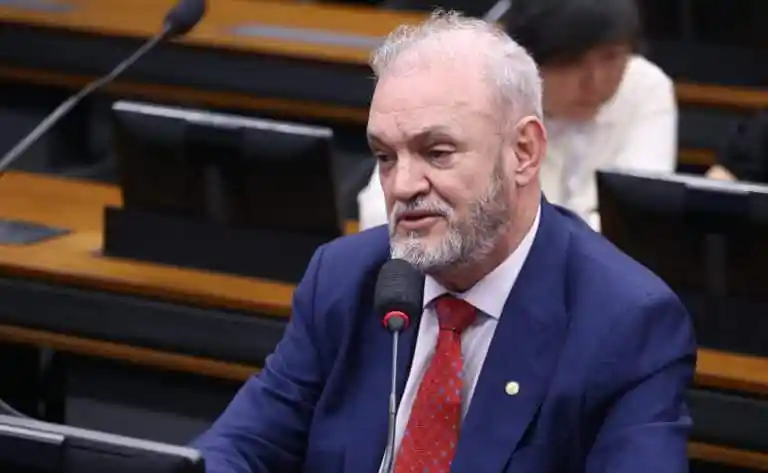 Homem de terno falando ao microfone durante audiência em comissão parlamentar.