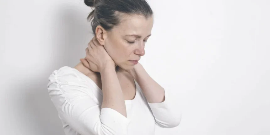 Mulher com expressão de dor segurando o pescoço com as duas mãos, em fundo branco.