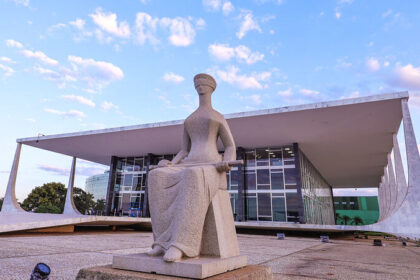 Estátua da Justiça em frente ao prédio do Supremo Tribunal Federal em Brasília, com céu azul ao fundo.