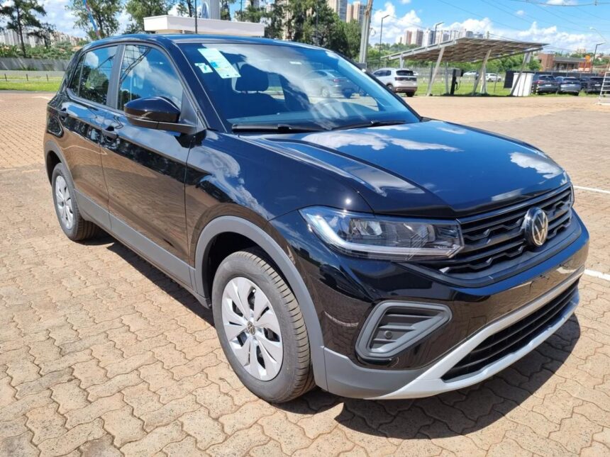 SUV T-cross compacto preto estacionado em área externa, com design moderno, faróis afilados e grade frontal com logotipo da Volkswagen. O veículo está em um pátio pavimentado, com outros carros e prédios ao fundo.