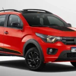 Carro compacto vermelho com detalhes em preto, modelo com visual aventureiro, exibido em fundo neutro. O veículo possui quatro portas, rodas escuras e elementos de design esportivo, com destaque para a frente e laterais. Fiat Mobi