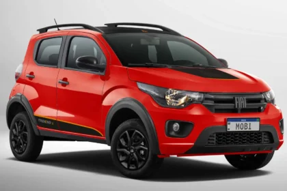 Carro compacto vermelho com detalhes em preto, modelo com visual aventureiro, exibido em fundo neutro. O veículo possui quatro portas, rodas escuras e elementos de design esportivo, com destaque para a frente e laterais. Fiat Mobi
