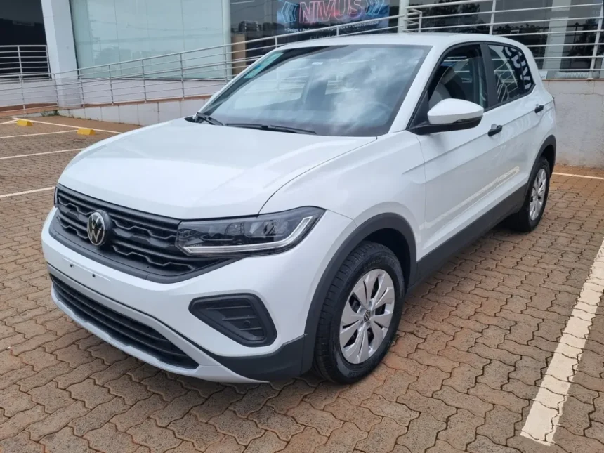 Imagem de um SUV branco Volkswagen T-Cross estacionado em área pavimentada, em frente a um prédio comercial com rampa de acessibilidade e corrimãos. O veículo aparece em destaque, visto de frente e lateralmente.
