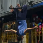 Pessoa realiza uma apresentação de tecido acrobático de cabeça para baixo em um espaço cultural. A imagem destaca a participação de artistas com deficiência nas artes circenses e na cultura inclusiva.
