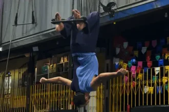 Pessoa realiza uma apresentação de tecido acrobático de cabeça para baixo em um espaço cultural. A imagem destaca a participação de artistas com deficiência nas artes circenses e na cultura inclusiva.