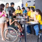 Carreta da Inclusão: Pessoa em cadeira de rodas é atendida por profissionais durante uma ação da Carreta da Inclusão. Outras pessoas aguardam atendimento em um espaço montado para oferecer serviços gratuitos e orientações às pessoas com deficiência e suas famílias.
