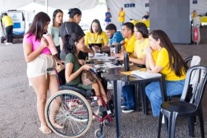 Carreta da Inclusão: Pessoa em cadeira de rodas é atendida por profissionais durante uma ação da Carreta da Inclusão. Outras pessoas aguardam atendimento em um espaço montado para oferecer serviços gratuitos e orientações às pessoas com deficiência e suas famílias.
