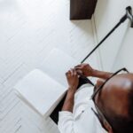 Vista superior de um homem de óculos lendo um livro em Braille, com uma bengala ao lado.