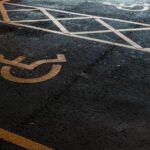 Vaga de estacionamento reservada para pessoas com deficiência, identificada pelo símbolo de acessibilidade pintado sobre o asfalto, com faixas de sinalização delimitando a área de circulação.