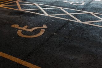 Vaga de estacionamento reservada para pessoas com deficiência, identificada pelo símbolo de acessibilidade pintado sobre o asfalto, com faixas de sinalização delimitando a área de circulação.