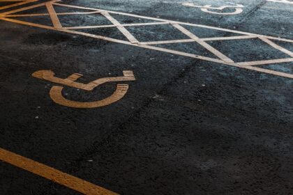 Vaga de estacionamento reservada para pessoas com deficiência, identificada pelo símbolo de acessibilidade pintado sobre o asfalto, com faixas de sinalização delimitando a área de circulação.