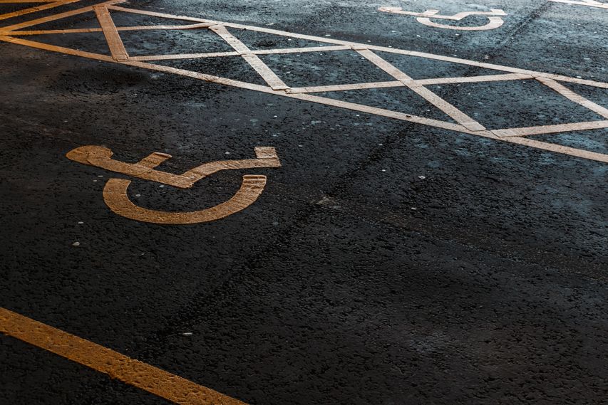 Vaga de estacionamento reservada para pessoas com deficiência, identificada pelo símbolo de acessibilidade pintado sobre o asfalto, com faixas de sinalização delimitando a área de circulação.